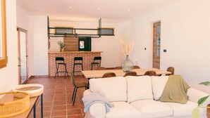 A modern living room with a white sofa, a dining table, and a kitchen area with a brick backsplash. - Country House in Torrecaballeros with Mountain Views, Private Pool, and Wi-Fi (Torrecaballeros)