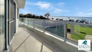 A balcony with a glass railing overlooking a grassy area and a body of water. - Hamptons Retreat by the Bay - Cowes Coastal Escape (Cowes)