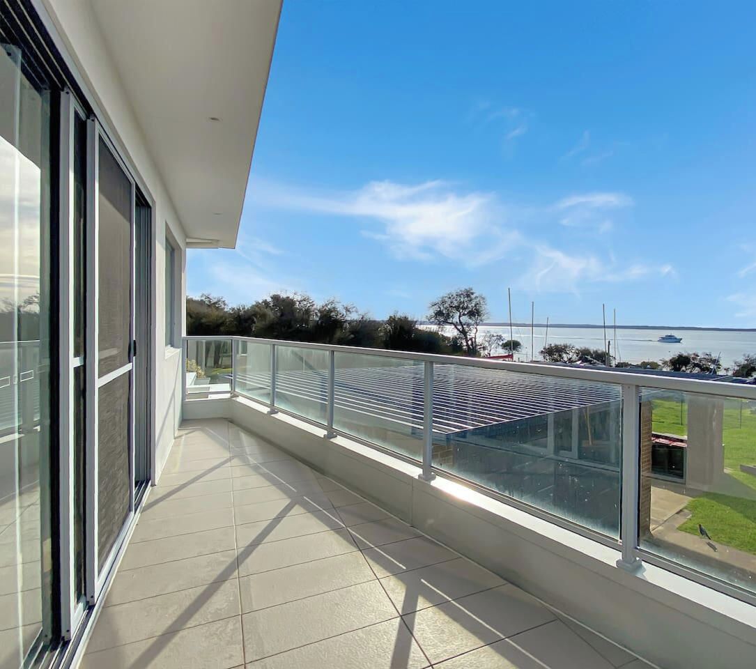 A balcony with a glass railing overlooking a grassy area and a body of water.