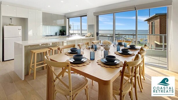A modern kitchen and dining area with a large island, wooden chairs, and a view of the sea. - Hamptons Retreat by the Bay - Cowes Coastal Escape (Cowes)