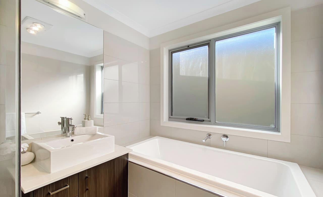 Een moderne badkamer met een grote spiegel, een witte wastafel en een bad.