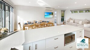 A modern kitchen with a central island, a dining area with a view of the sea, and a living area with a sofa and cushions. - Hamptons Retreat by the Bay - Cowes Coastal Escape (Cowes)