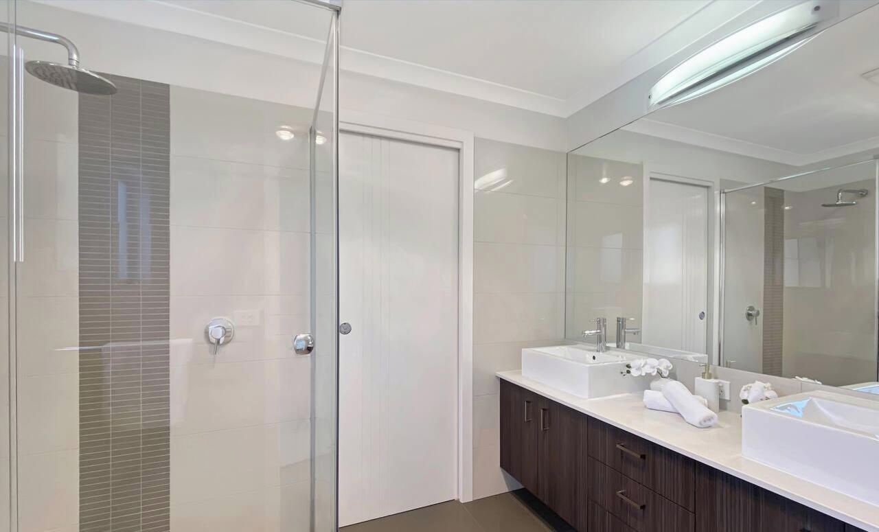 A modern bathroom with a glass shower enclosure, a double sink vanity, and a large mirror.