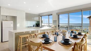 A modern kitchen and dining area with a large island, wooden chairs, and a view of the sea.
