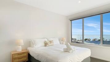 A bedroom with a large window, a bed, a nightstand, and a lamp.