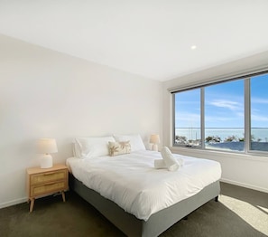 A bedroom with a large window, a bed, a nightstand, and a lamp.