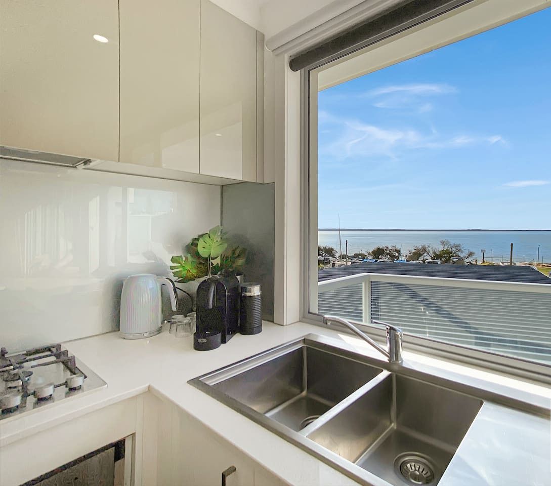 A modern kitchen with a large window overlooking a coastal view, including a marina and the sea.