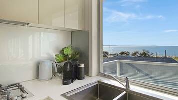 A modern kitchen with a large window overlooking a coastal view, including a marina and the sea.