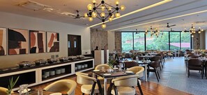 A spacious restaurant with high ceilings, modern chandeliers, and large windows offering a view of the outdoors. - Ullasa by Momentum (Udaipur)