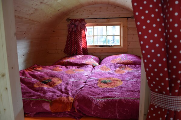 A cozy room with wooden walls, a window with curtains, and a bed with a floral bedspread.