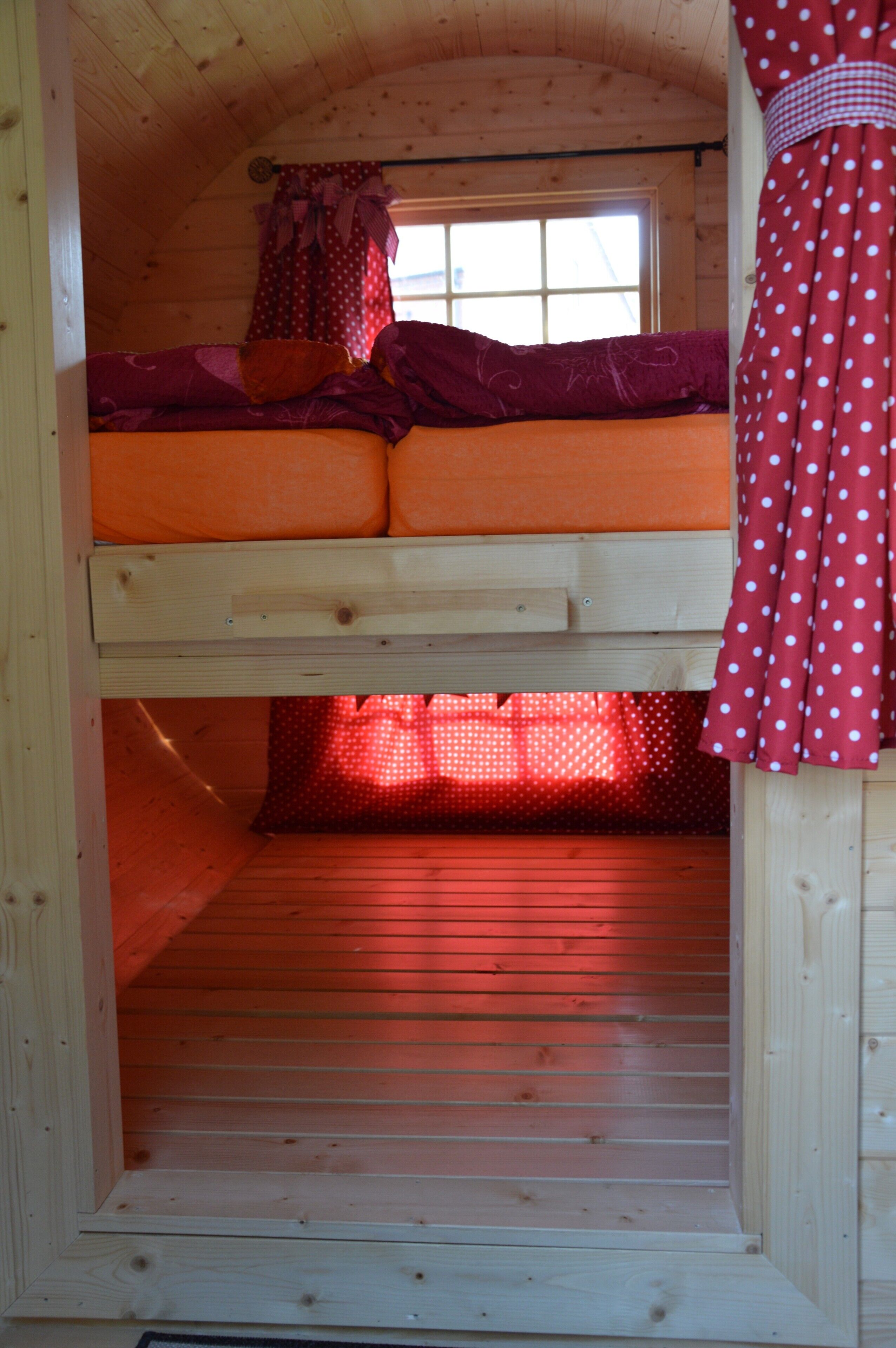 A bunk bed with a window above, curtains, and a wooden floor.