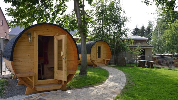 Cabañas cilíndricas de madera con puertas abiertas, un sendero de ladrillo y una zona verde.