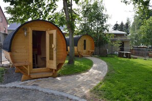 Wooden cylindrical cabins with open doors, a brick pathway, and a grassy area.