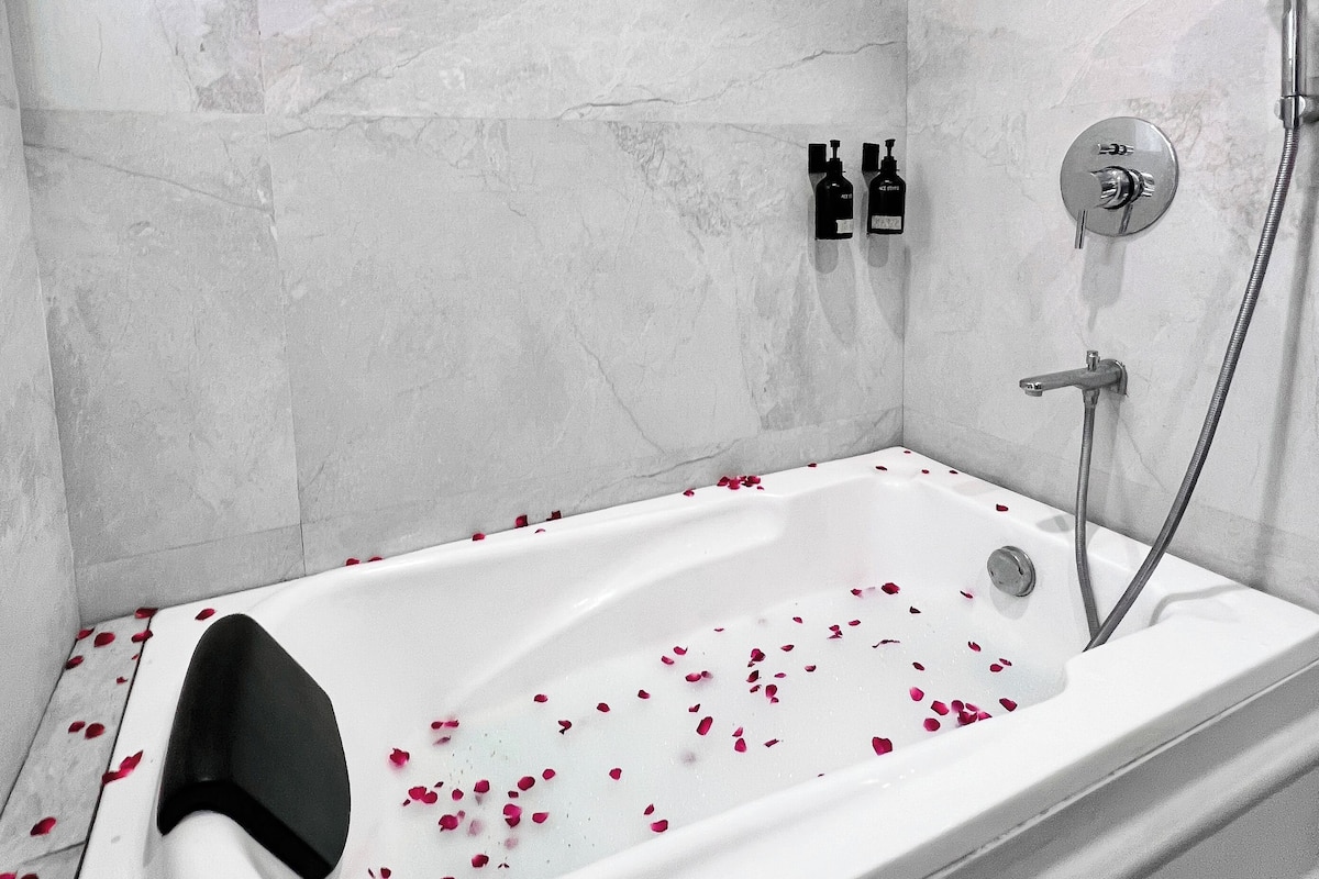 A modern bathroom with a bathtub, shower, and marble walls.