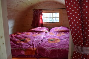 A wooden cabin room with a bed, a window, and a curtain.