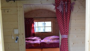 Een klein houten vakantiehuisje met een slaapzolder, een ladder en een raam met gordijnen.