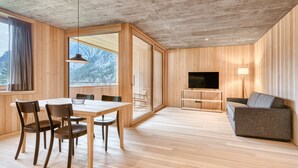 A modern living room with a wooden floor, a dining table with chairs, a sofa, a TV, and a large window with a mountain view. - Studa 29 - Studa 5 in Brand (Brand)