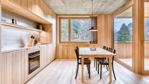 A modern kitchen with wooden cabinets, a dining table, and chairs. There is a large window providing a view of trees and mountains. - Studa 29 - Studa 5 in Brand (Brand)