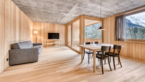 Ein modernes Interieur mit Holzboden, einer Couch, einem Esstisch mit Stühlen, einem Fernseher und einem großen Fenster mit Bergblick.