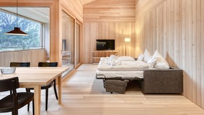 Un intérieur moderne avec un plafond en bois, un coin repas comprenant une table et des chaises, un lit avec des oreillers et un téléviseur posé sur un meuble en bois.