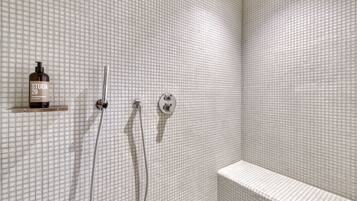 A shower area with a tiled wall, a showerhead, a handheld shower, and a bottle of shampoo on a shelf.