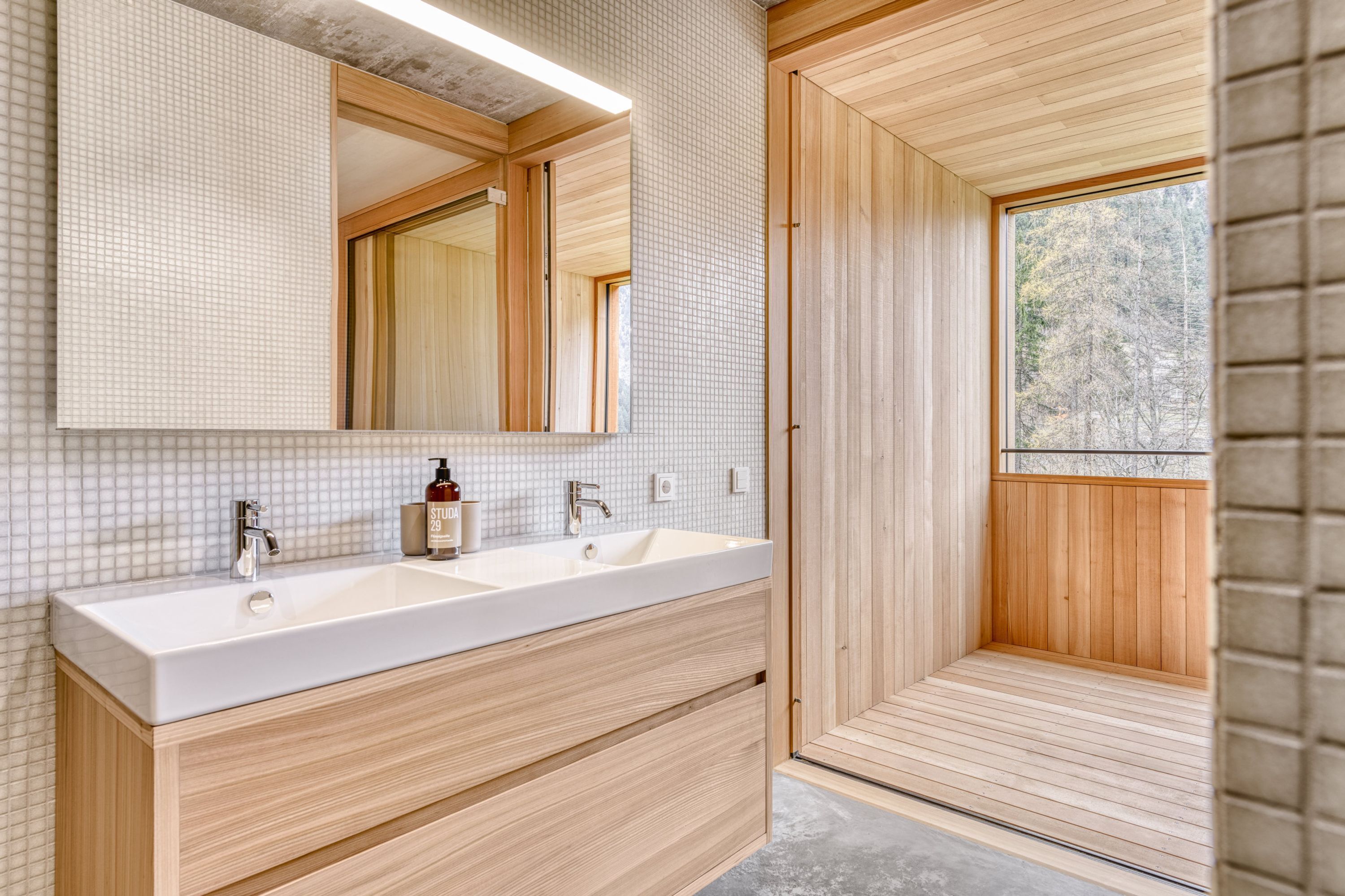 Een moderne badkamer met een grote spiegel, twee wastafels, houten kastjes en een sauna.