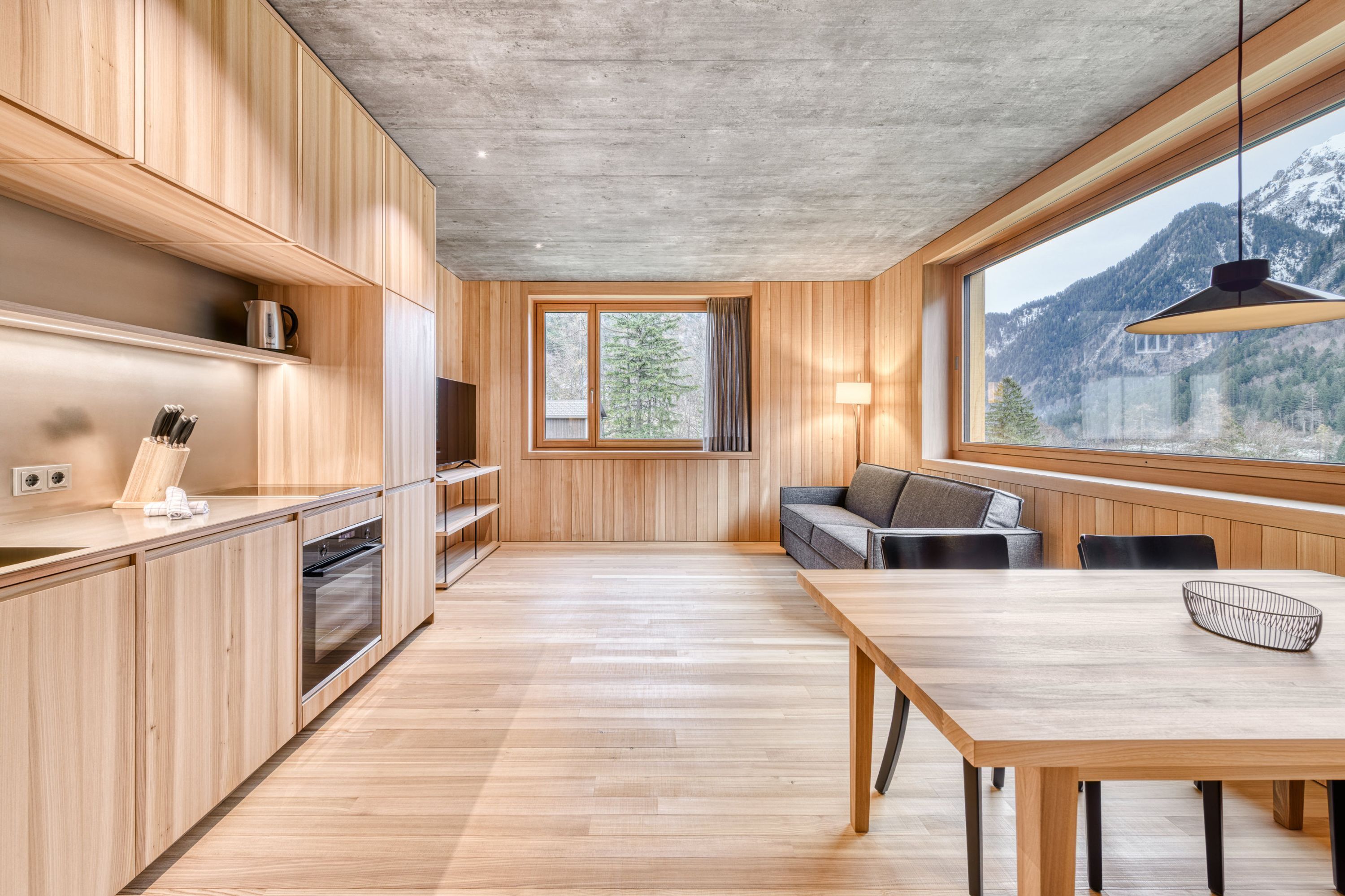 A modern kitchen with wooden cabinets, a built-in oven, and a large window overlooking a mountainous landscape.