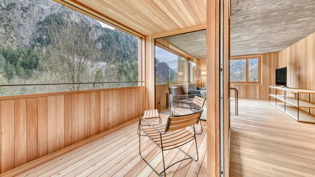 A modern interior with wooden paneling, a dining area with metal chairs, and large windows offering mountain views. - Studa 29 - Studa 2 in Brand (Brand)