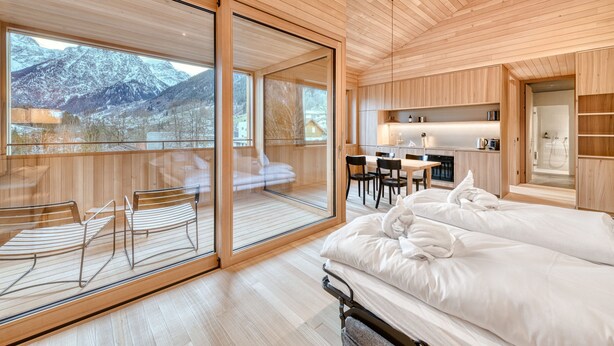 A modern hotel room with a large sliding glass door leading to a balcony, a cozy bed, a small kitchen area, and a seating area with chairs. - Studa 29 - Studa 10 in Brand (Brand)