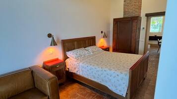 A bedroom with a wooden bed, a nightstand with a lamp, a leather sofa, and a brick floor.