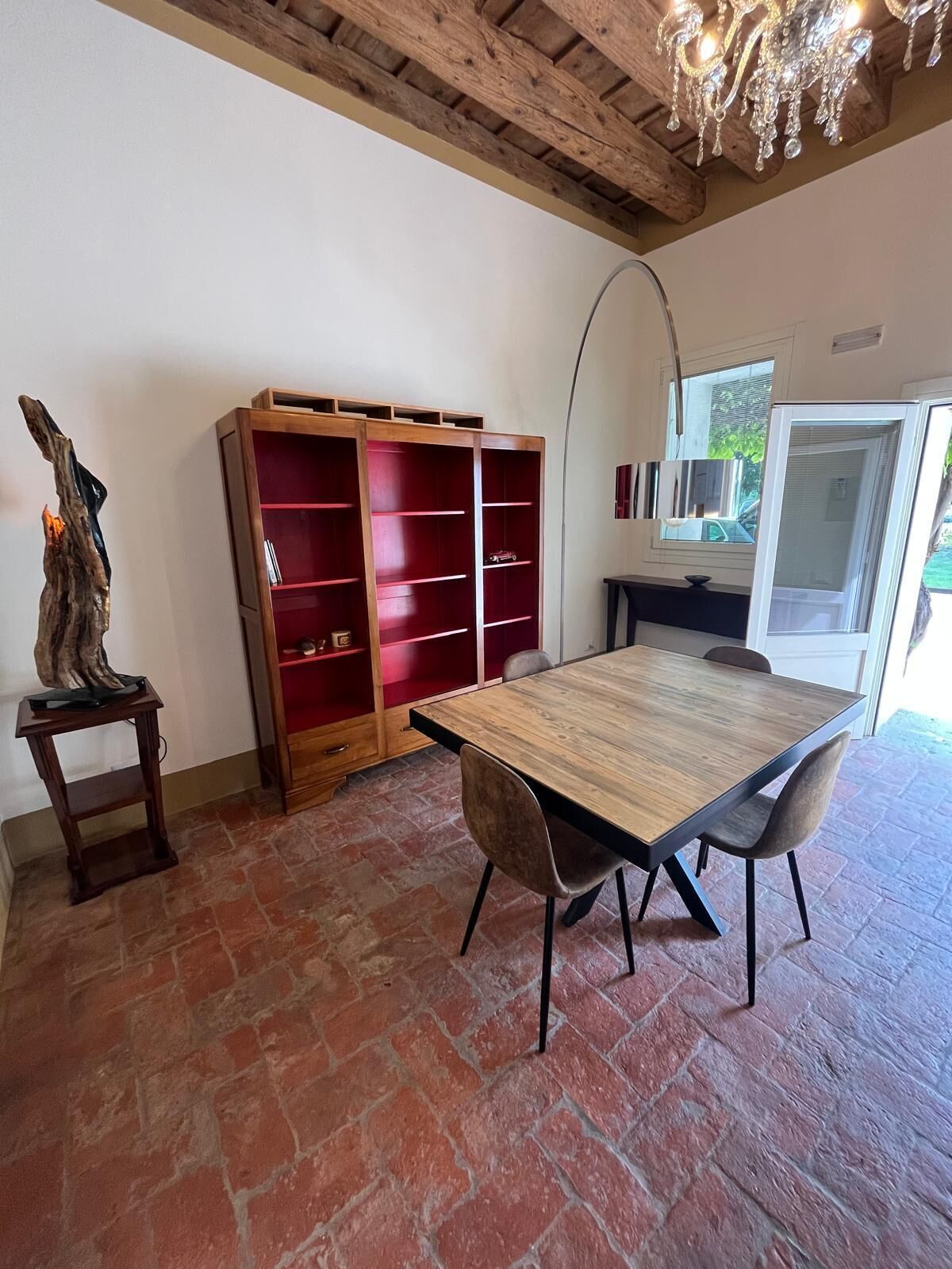 Uma sala de jantar com mesa e cadeiras de madeira, uma estante vermelha e teto rústico.