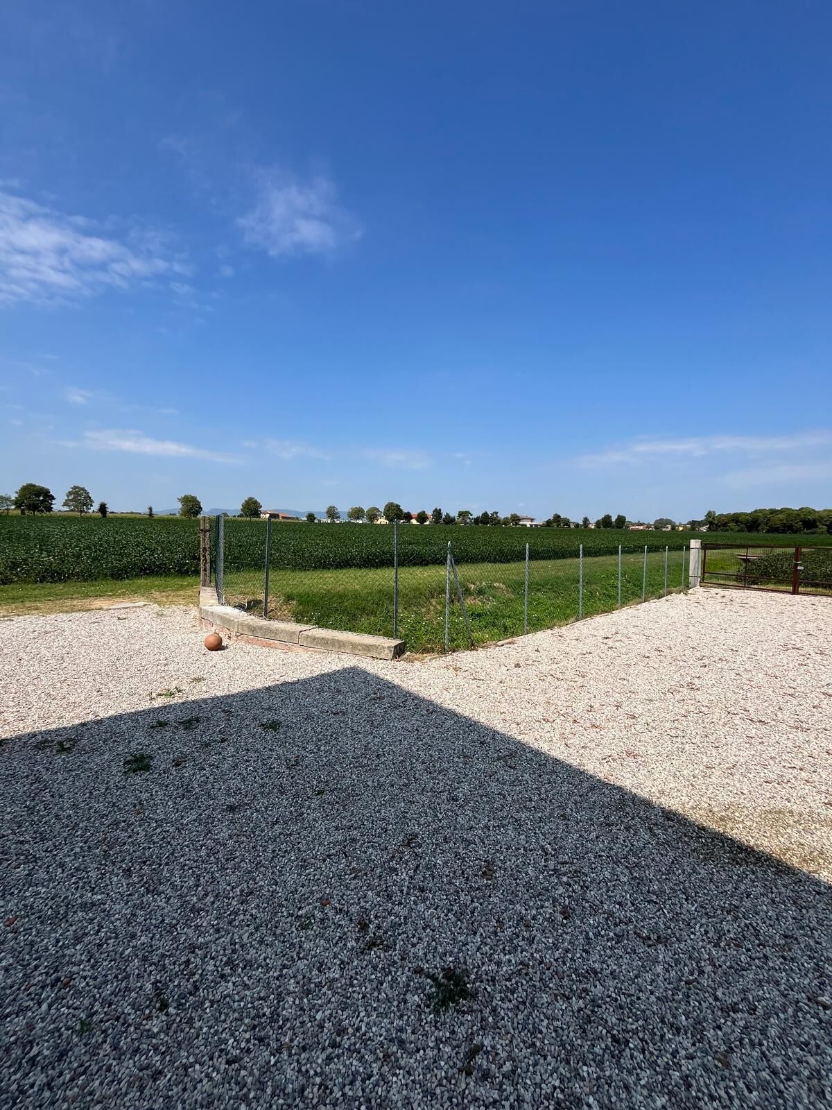 A gravel parking area with a fence and a field in the background.