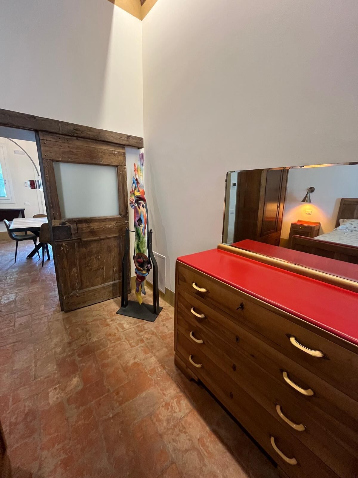 A room with a wooden dresser, a bed with a nightstand, and a mural on the wall.