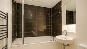 A modern bathroom with a glass-enclosed shower, a white bathtub, and a sink with a mirror above it. - Still Life Moorgate Deluxe (London)