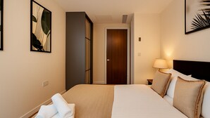 A hotel room with a neatly made bed, a bedside lamp, and a door leading to another room. - Still Life Moorgate Deluxe (London)