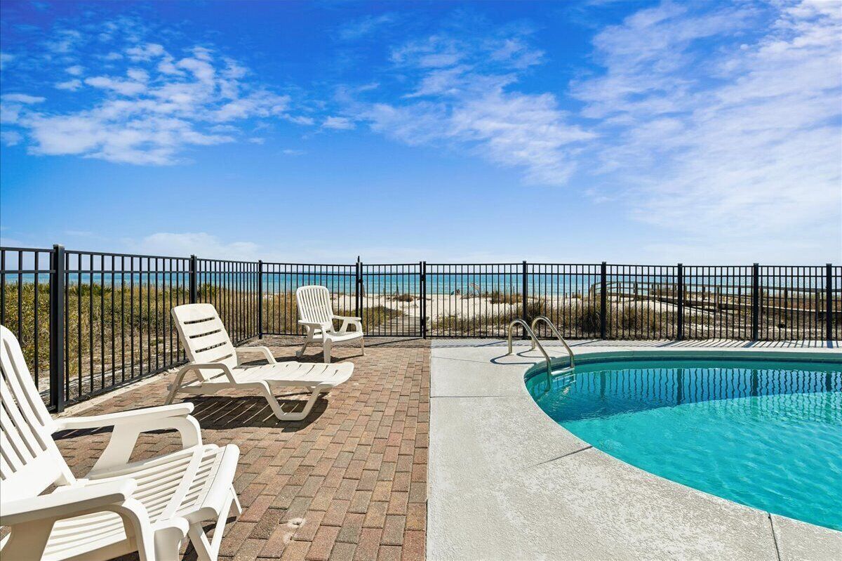A pool area with a clear view of the ocean, surrounded by a black fence and white lounge chairs.