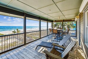 Un espace extérieur abrité, doté d’une terrasse en bois, d’une table avec des chaises et offrant une vue sur la plage et l’océan.