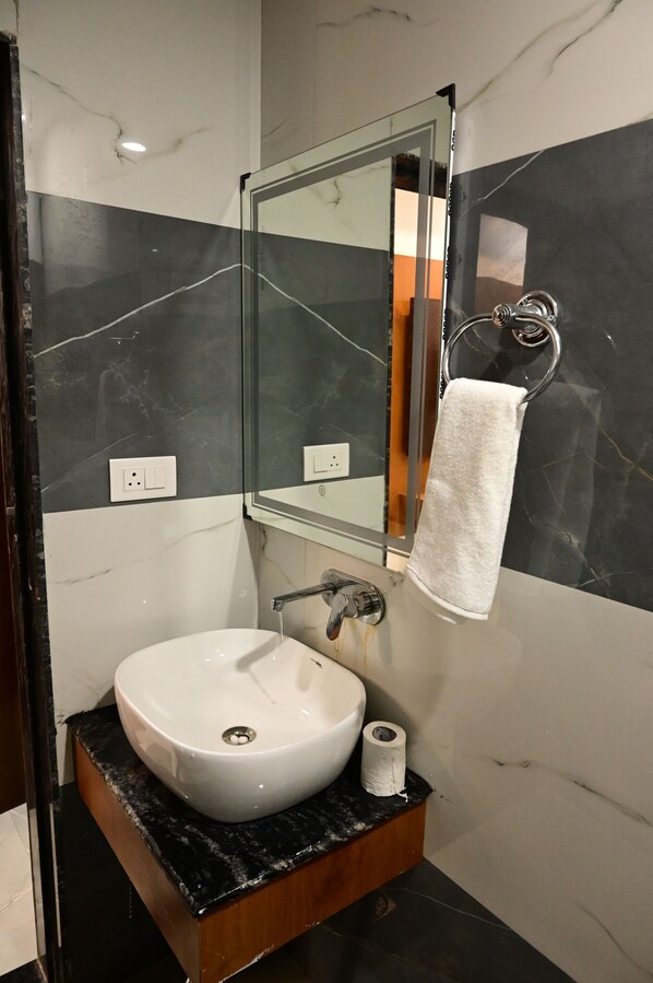 A bathroom with a white sink, a mirror, a towel rack, and a toilet paper roll.
