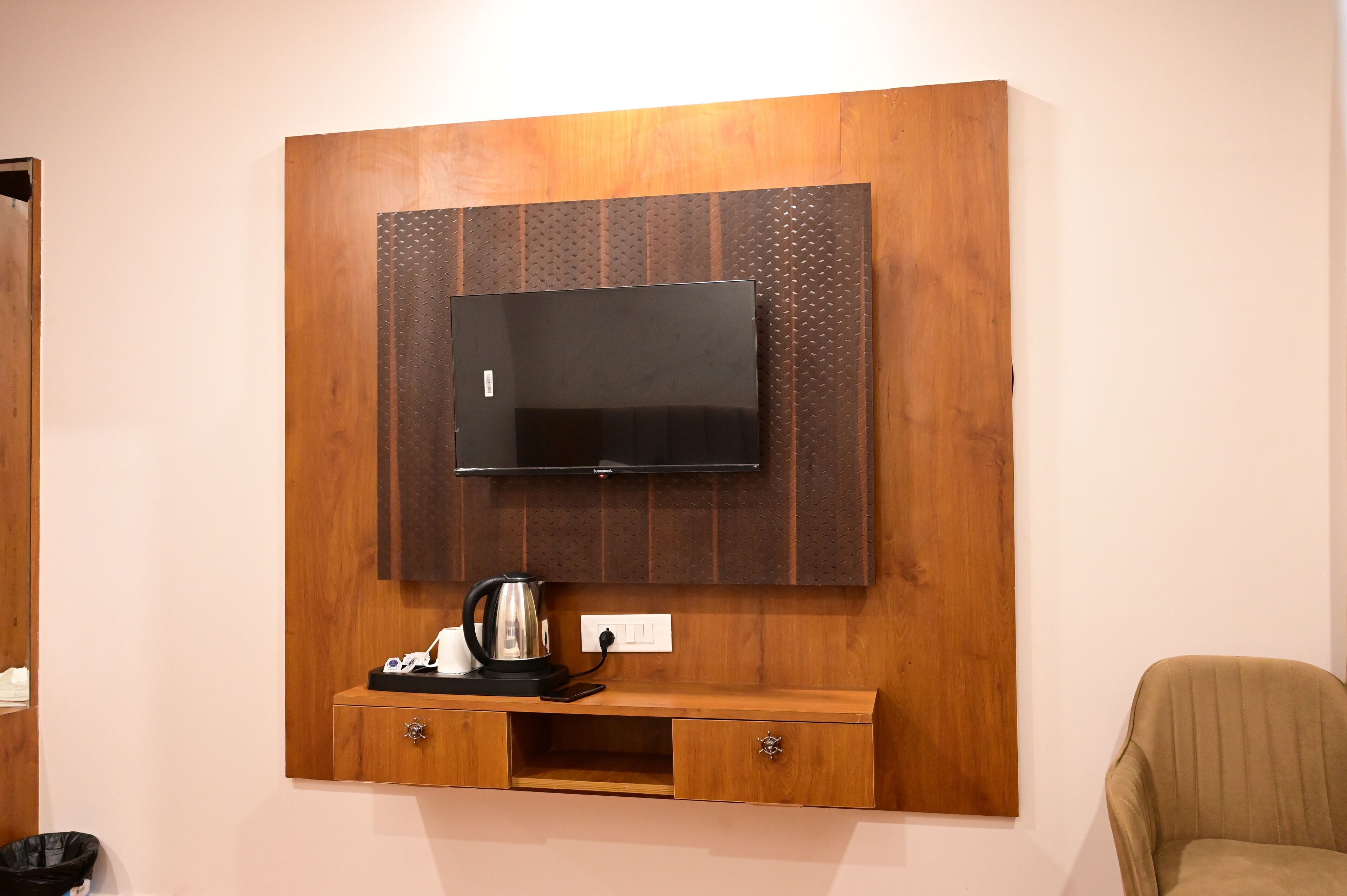 A wooden wall unit with a flat-screen TV, a coffee maker, and a power outlet.