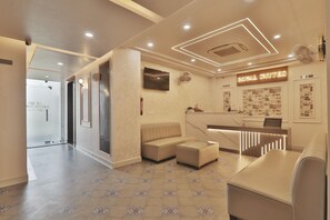 A hotel reception area with a reception desk, a sofa, and a television mounted on the wall.