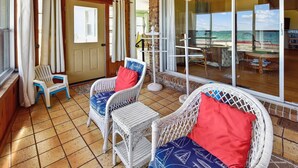 A covered outdoor seating area with wicker chairs and a table, a door leading inside, and a view of the sea through large glass doors. - Welcome to Easy Does It! (St. George Island)