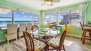A dining area with a glass table and wicker chairs, large windows with ocean views, and a ceiling fan. - Welcome to Easy Does It! (St. George Island)