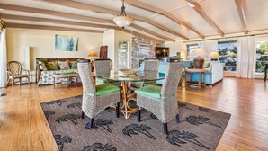 A spacious living area with a high ceiling, wooden flooring, and a central glass table surrounded by wicker chairs with green cushions. - Welcome to Easy Does It! (St. George Island)