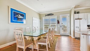 A dining area with a glass table and wooden chairs, a white door, and a kitchen area with a refrigerator. - Welcome to Salty Dawg! (Eastpoint)