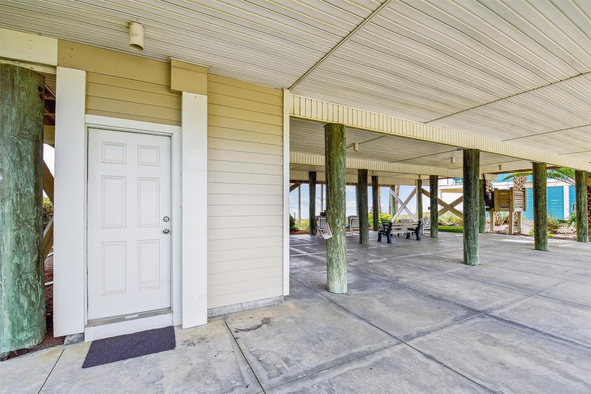 A covered outdoor area with a white door, concrete flooring, and wooden pillars.