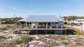 A beachfront house with a covered deck, outdoor seating, and a view of the beach.