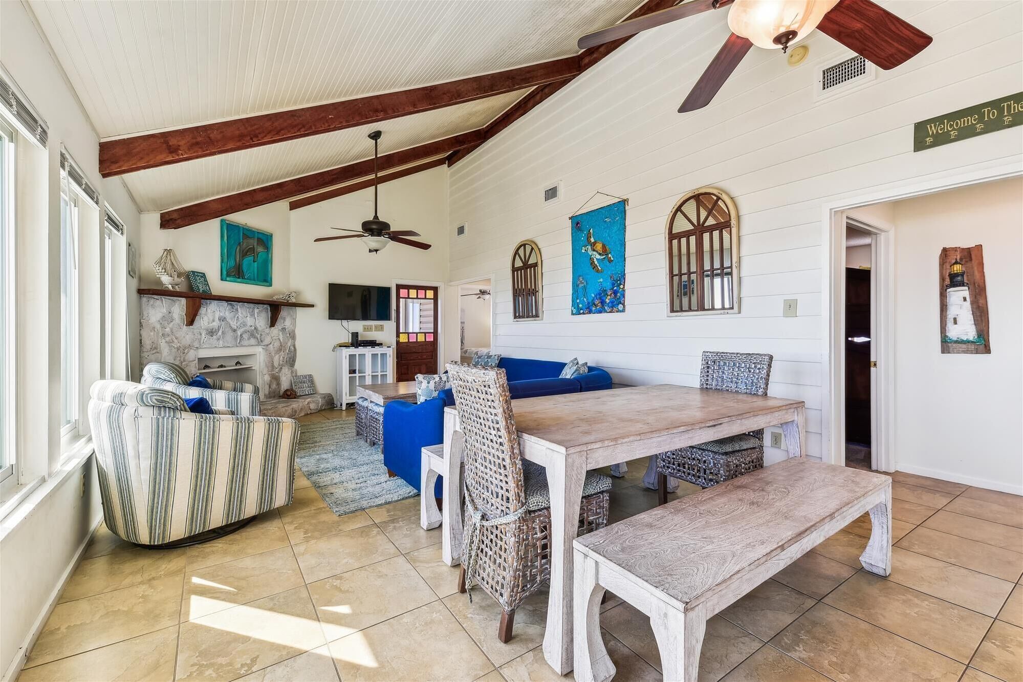 A spacious living room with a fireplace, a dining area with a wooden table and benches, and a ceiling fan.