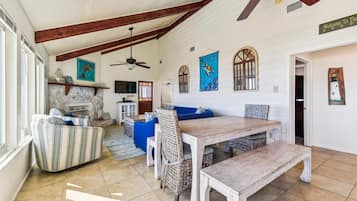 A spacious living room with a fireplace, a dining area with a wooden table and benches, and a ceiling fan.