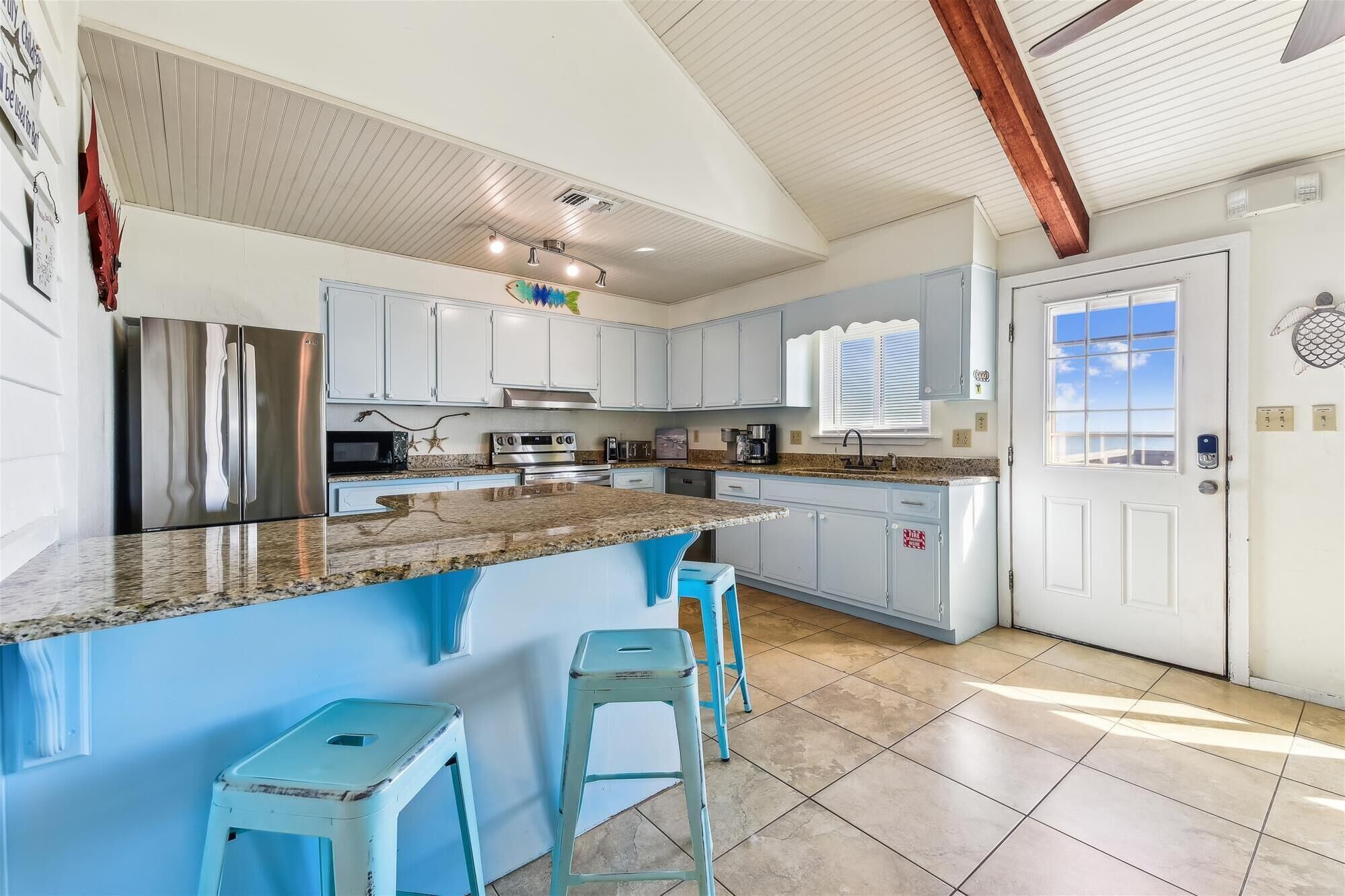 A spacious kitchen with a large island, white cabinets, and a view to the outside.