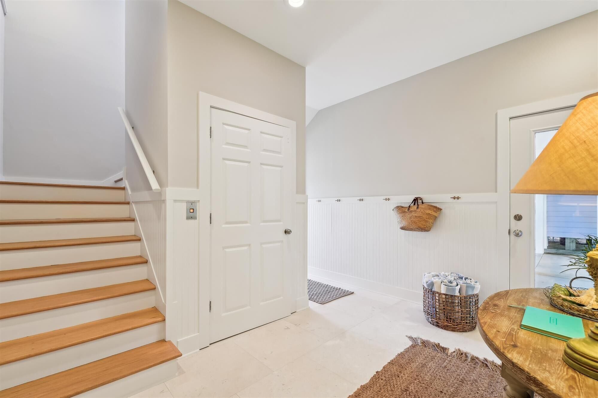 A clean, modern hallway with a wooden staircase, a white door, and a basket hanging on the wall.